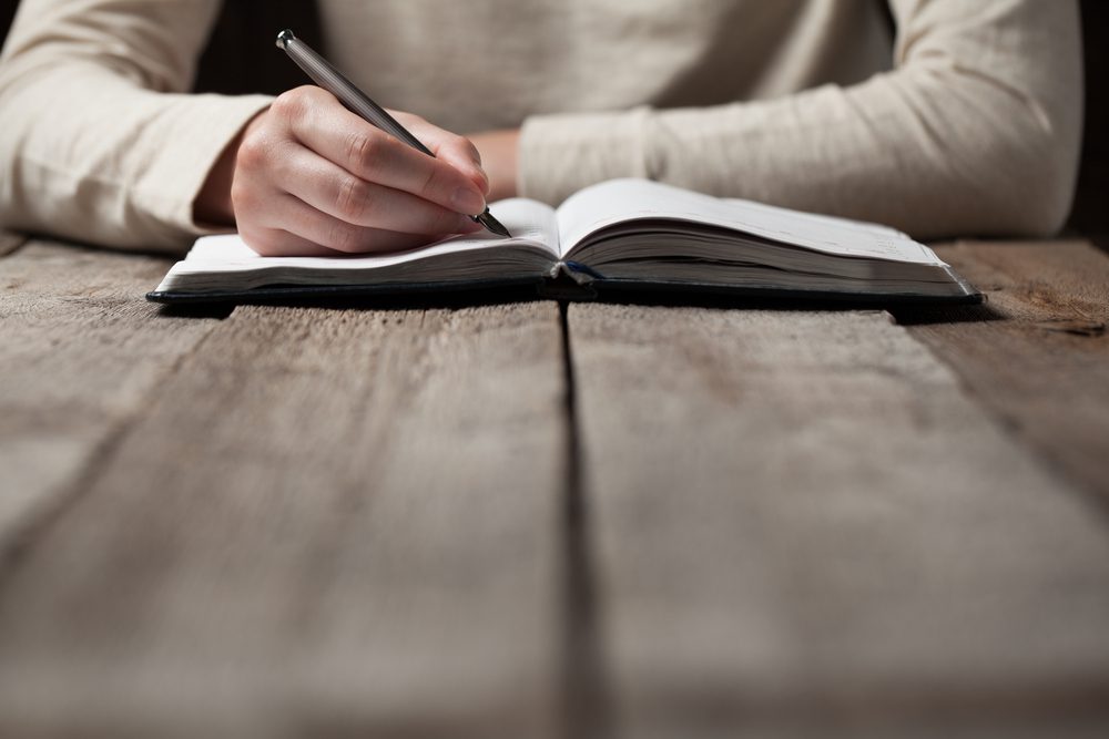 writing contemplatively on a notebook.